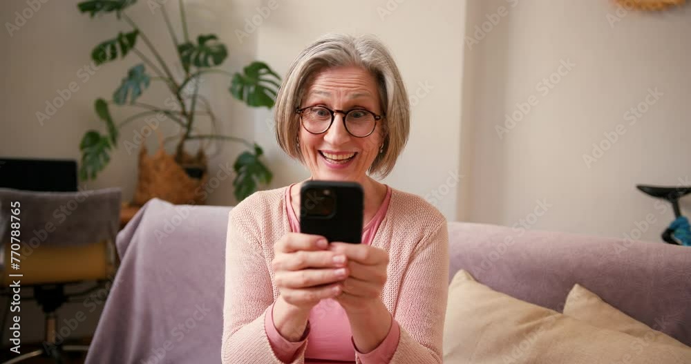 Happy mature old 60s woman, older middle aged female holding smartphone using mobile app, texting message while chatting with friends with cell phone on couch at home. Happy laugh, having fun Happy mature old 60s woman, older middle aged female holding smartphone using mobile app, texting message while chatting with friends with cell phone on couch at home. Happy laugh, having fun