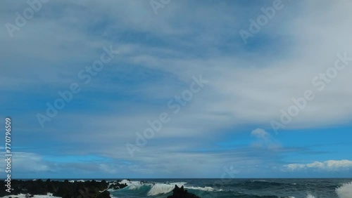 Tilt shot of the waves slowly splashing on black lava rocks. Cloudy day at the volcanic beach in Keanae Penisula, Maui. photo