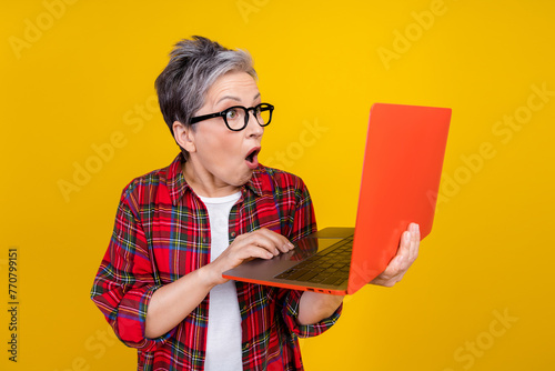Photo of impressed grandmother use wireless laptop open mouth cant believe isolated on yellow color background