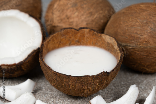 Coconut milk in coconut shell and half coconut, chopped flesh on grey background