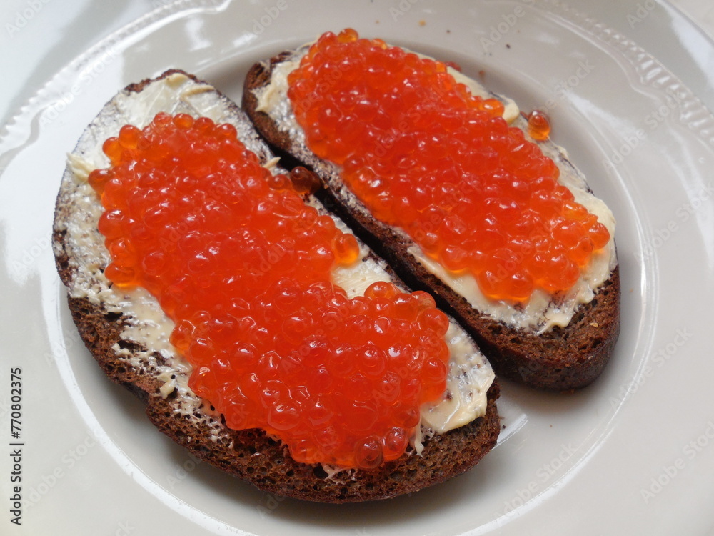 The seafood delicacy red caviar is beautifully served on black bread and butter. The seafood delicacy red caviar is beautifully served on black bread and butter.