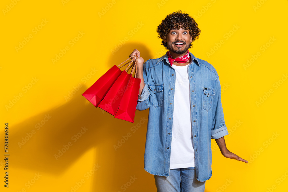 Photo portrait of handsome young guy hold excited shopping bags dressed stylish jeans garment red scarf isolated on yellow color background Photo portrait of handsome young guy hold excited shopping bags dressed stylish jeans garment red scarf isolated on yellow color background