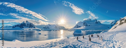 a group of penguins frolicking on the snow-covered ground against the backdrop of majestic blue mountains, tranquil waters dotted with floating icebergs, and the radiant sun shining brightly photo