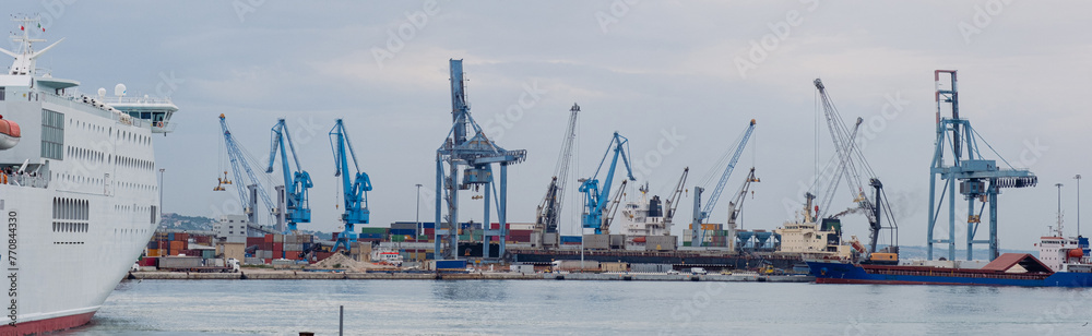 Panoramic View of the port with many port cranes and a huge liner entering the port. 