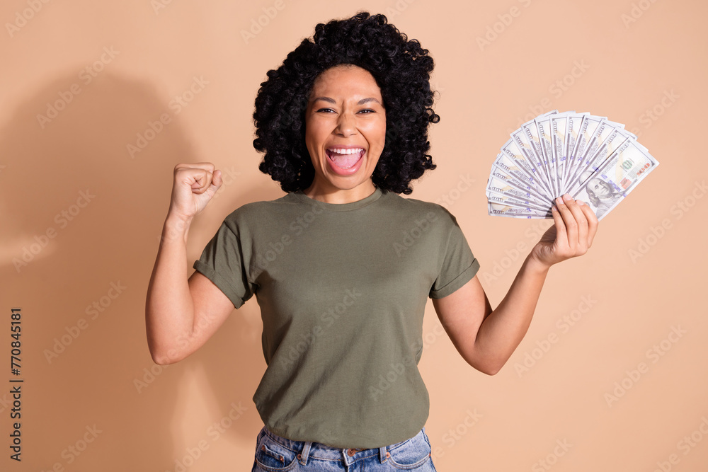 Photo of overjoyed woman with afro hairstyle wear khaki t-shirt hold money clenching fist win gambling isolated on beige color background Photo of overjoyed woman with afro hairstyle wear khaki t-shirt hold money clenching fist win gambling isolated on beige color background