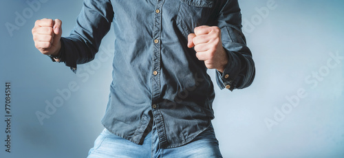 A man in a blue shirt and jeans is holding and clenching his fists up in the air. on blue background photo