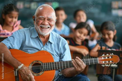A senior teacher in blue shirt teaches children to play the acoustic guitar at school during a music lesson.