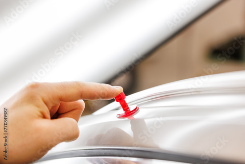 Hand pressing red pin on car roof. Dent removal concept