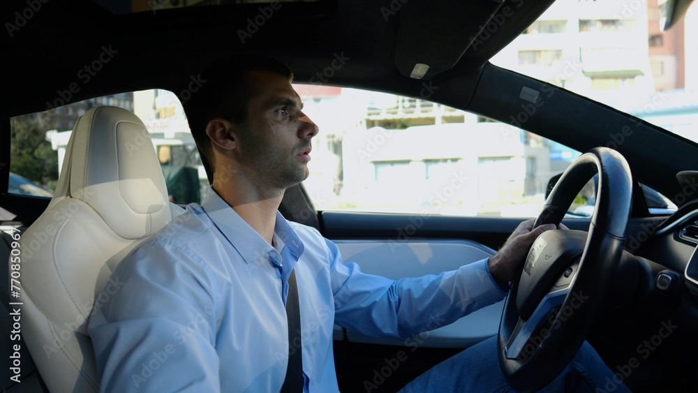 Profile of handsome businessman driving a modern electric car at urban road. Male successful entrepreneur riding on electrical vehicle at city. Young man commuting to work at sunny day. Slow motion Profile of handsome businessman driving a modern electric car at urban road. Male successful entrepreneur riding on electrical vehicle at city. Young man commuting to work at sunny day. Slow motion
