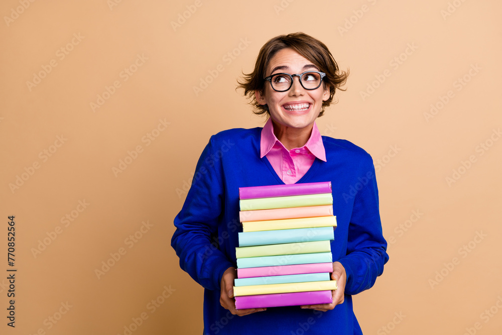 Photo of clever cheerful lady toothy smile hold pile stack book look empty space isolated on beige color background Photo of clever cheerful lady toothy smile hold pile stack book look empty space isolated on beige color background