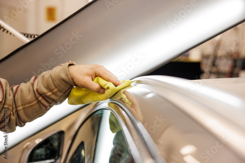 Person cleaning car with yellow cloth on hood and rims
