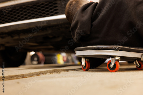 Man rolling on skateboard under car for automotive maintenance