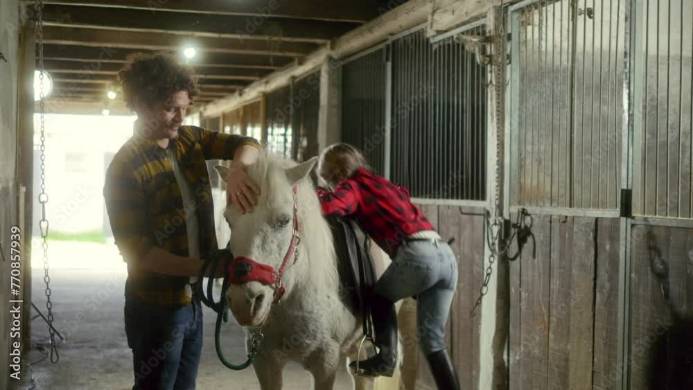 Little girl child climbs up on to a horse in a barn on the family ranch Little girl child climbs up on to a horse in a barn on the family ranch