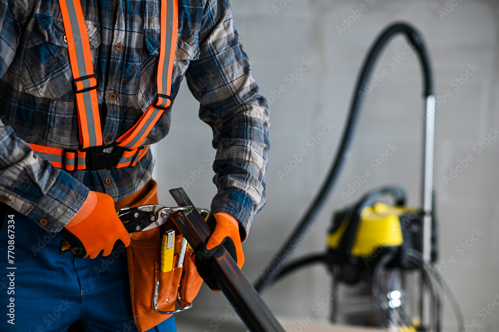 a construction worker in overalls, gloves and a tool belt cuts an iron profile for plasterboard with scissors a construction worker in overalls, gloves and a tool belt cuts an iron profile for plasterboard with scissors