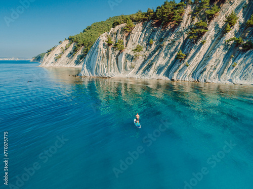 Paddle boarding in Mediterranean sea with mountain coastline. Aerial drone view