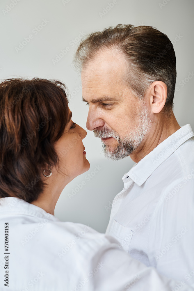 Side view portrait of mature couple in love hugging and going to kiss on grey backdrop, closeness