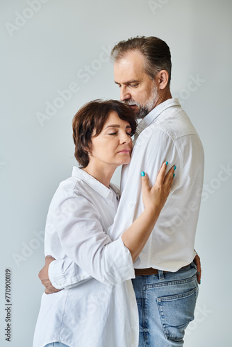 Attractive middle aged woman hugging mature man in white shirt with love on grey background