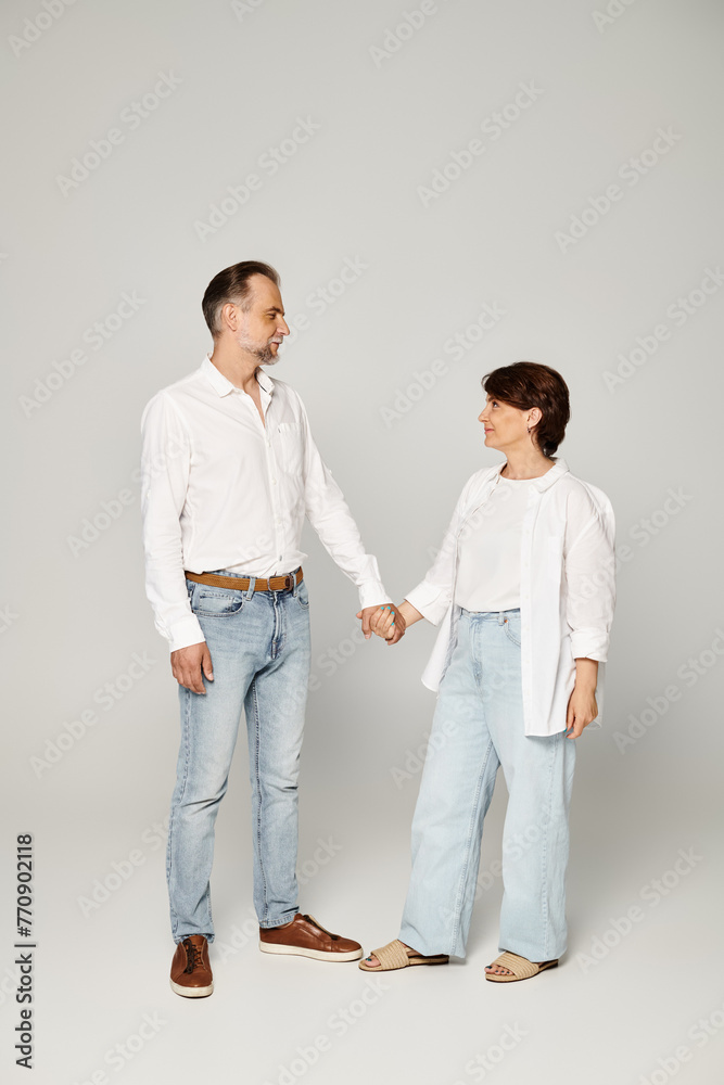 Full length shot of mature beautiful couple standing on grey background and looking at each other Full length shot of mature beautiful couple standing on grey background and looking at each other