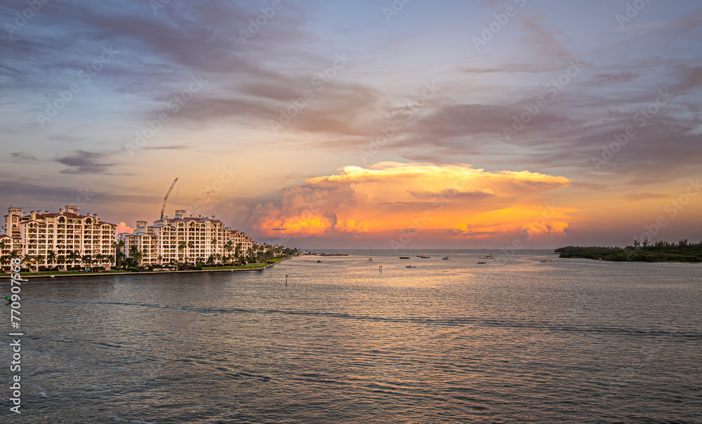 Miami, Florida, USA - July 29, 2023: Mushroom orange sunset cloud separates luxury condominiums along Fisher Island shoreline and Virginia Key island under evening sky. Small boats