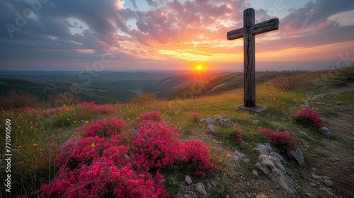   A hilltop cross with pink flowers in the foreground and sunset in the background photo