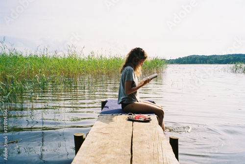 Young woman sitting on wooden pier and reading book photo