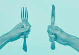 Hands holding cutlery with blue background, one hand with fork, other hand with knife Dining utensils concept