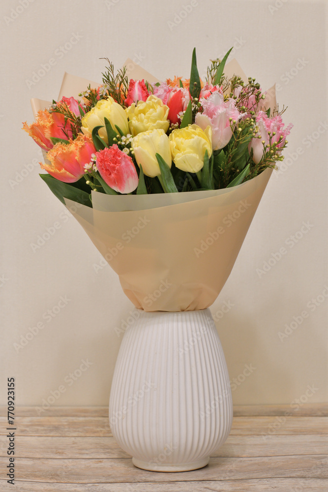 A bouquet of flowers in ceramic vase stands on a table in the room