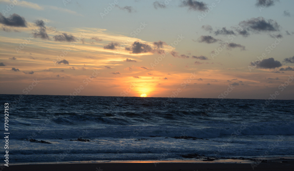 sunset at sea, with orange sky and the sun setting on the beach horizon