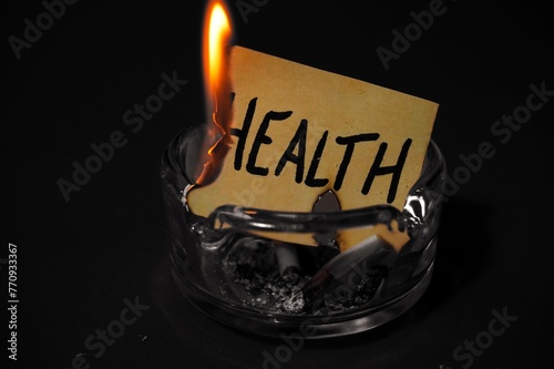 piece of paper with the writing "health" burning due to cigarette smoke in an ashtray, concept of "smoking kills"
