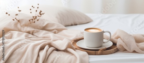 A coffee cup rests on a wooden tray placed on a bed, surrounded by cozy linens, creating a warm and inviting atmosphere