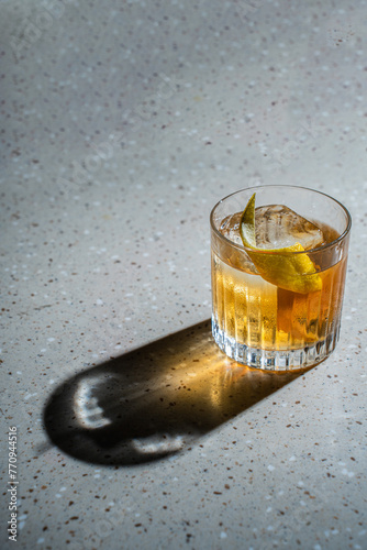Photography Yellow alcoholic cocktail with ice and lemon zest on a background of a concrete