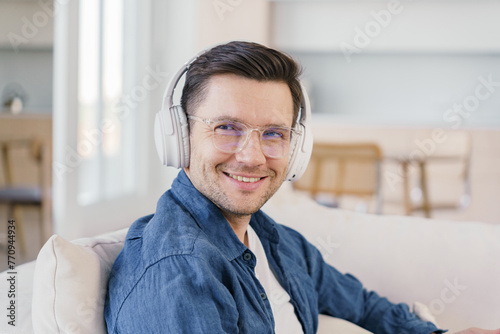 A man with a congenial smile enjoys his time in headphones, relaxing in a well-lit, modern living space.