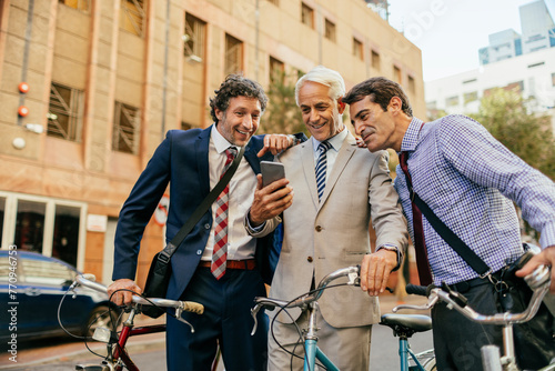 Three businessmen in suits looking at a smartphone together outdoors with bicycles photo