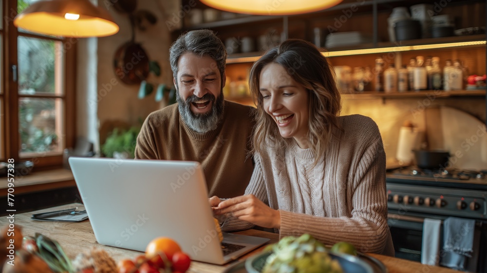 Smiling Couple Browsing on Laptop in Cozy Kitchen Setting Smiling Couple Browsing on Laptop in Cozy Kitchen Setting