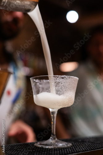 Bartender pours creamy white cocktail into coupe glass.
