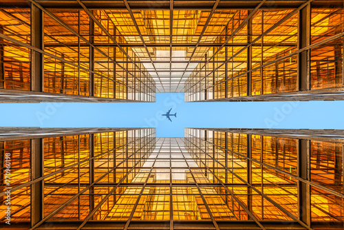 Looking up a golden symmetrical skyscraper to an flying aircraft in the very blue sky
