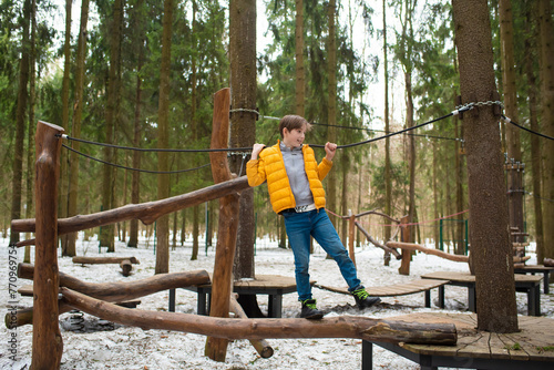 Boy in a yellow jacket  on a rope park in winter