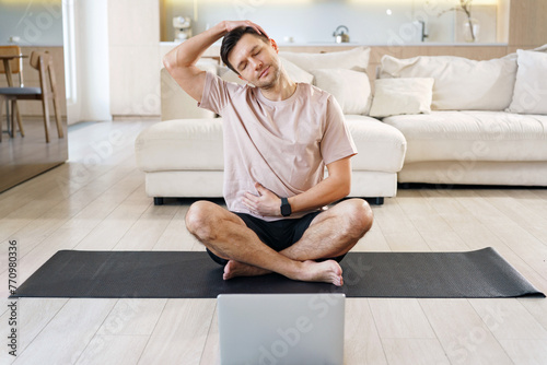 A man stretches on a yoga mat, easing neck tension during a wellness break, with a laptop suggesting a blend of work and health.