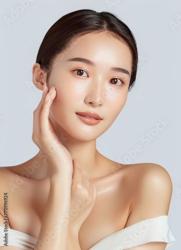 A beautiful asian woman with delicate skin, wearing white and touching her face in front of the camera on an isolated light gray background,generative ai