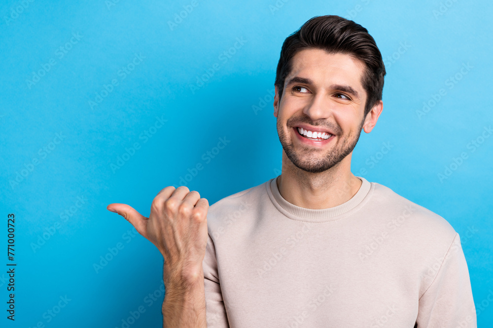 Photo of nice young man look direct finger empty space wear beige sweatshirt isolated on blue color background Photo of nice young man look direct finger empty space wear beige sweatshirt isolated on blue color background