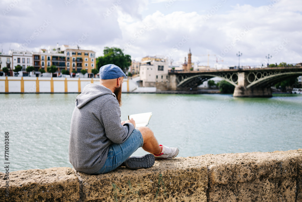 Young man writing in book while sitting near river Young man writing in book while sitting near river