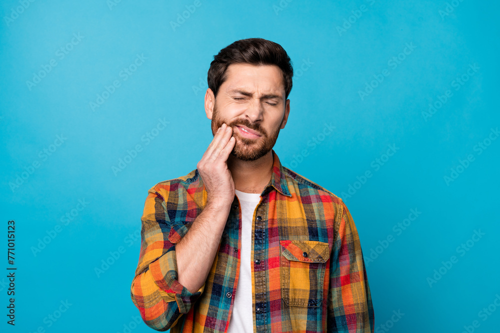 Photo portrait of nice young guy touch cheek suffer toothache dressed stylish checkered garment isolated on blue color background Photo portrait of nice young guy touch cheek suffer toothache dressed stylish checkered garment isolated on blue color background
