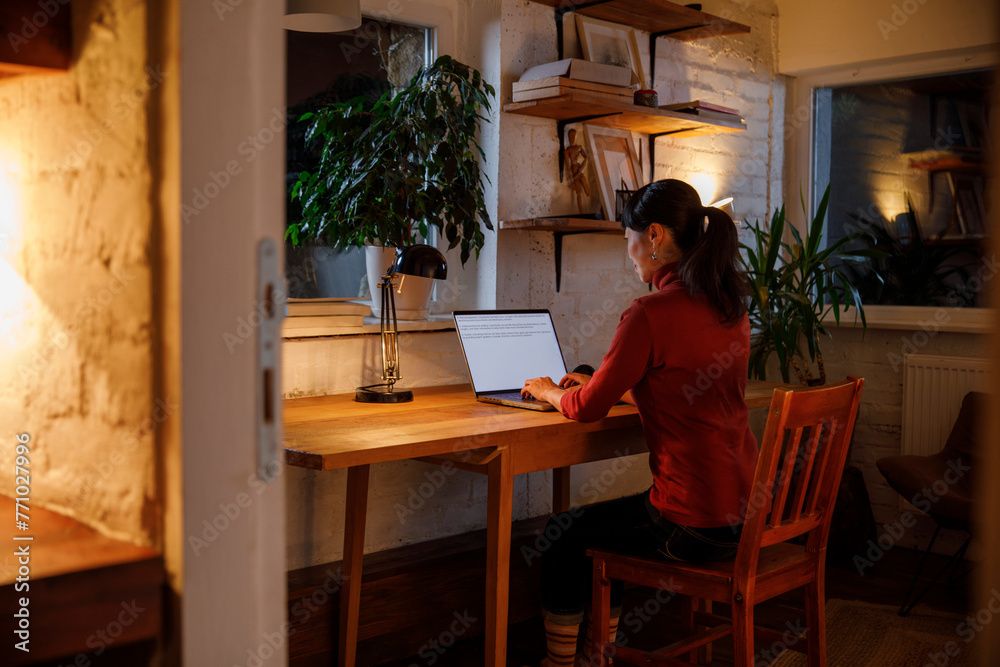 Businesswoman working on laptop at illuminated table in house Businesswoman working on laptop at illuminated table in house