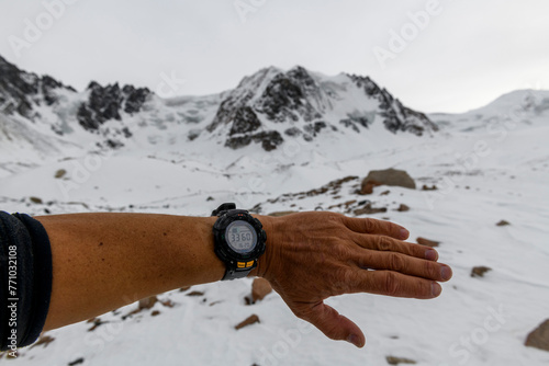 Man's hand with electronic watch showing altitude with snowy mountains on background. Climbing and hiking concept.