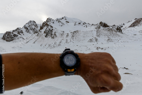 Man's hand with electronic watch showing altitude with snowy mountains on background. Climbing and hiking concept. photo