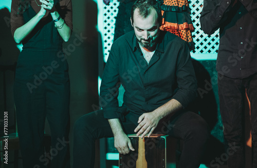 Stylish man sitting on Cajon box while drumming with band photo