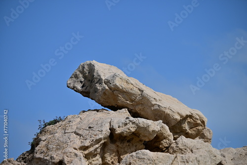 A big rock lies on top of a mountain at the coast of Benidorm-Spain in front of a blue sky.