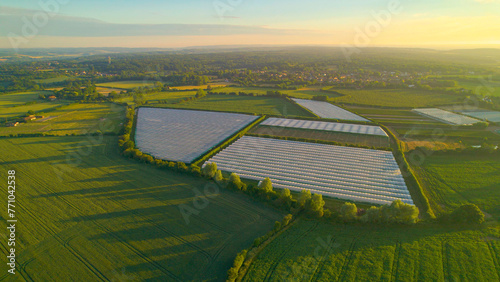 AERIAL: Golden sunset light shines on greenhouses amidst lush farming fields