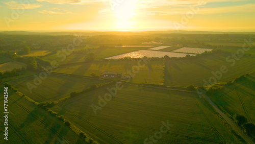 AERIAL, LENS FLARE: View towards the sun rising over scenic English countryside