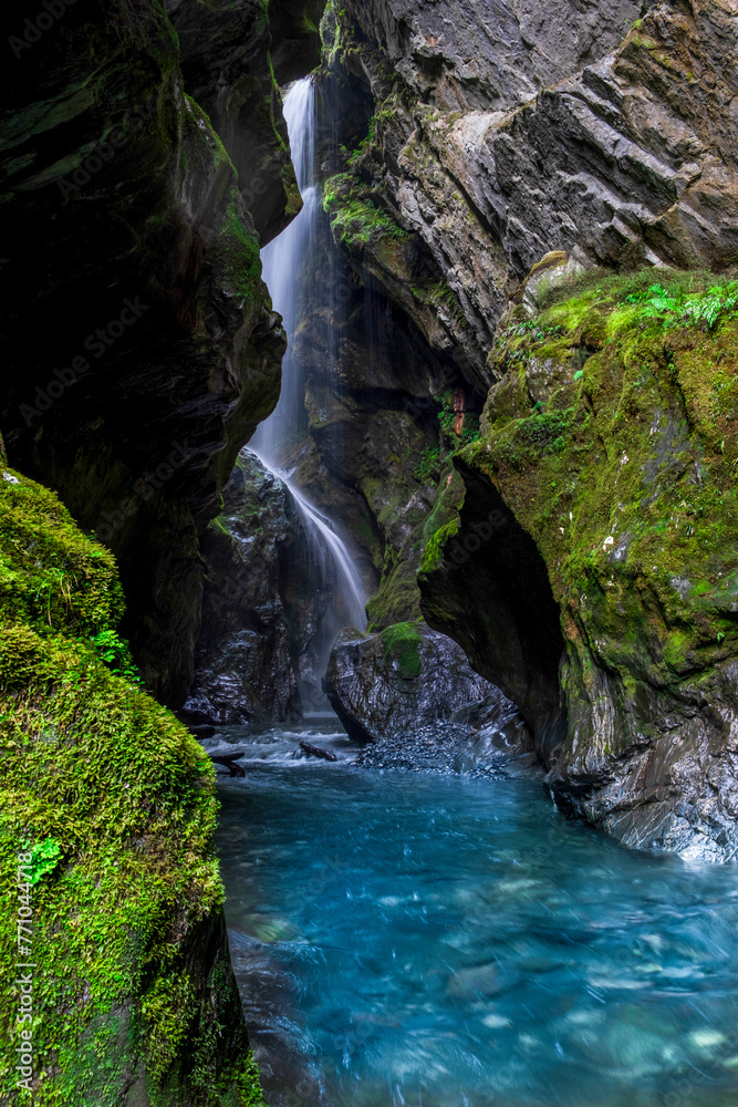 Upright view of Mossy cave with water fall and turquoise water Upright view of Mossy cave with water fall and turquoise water